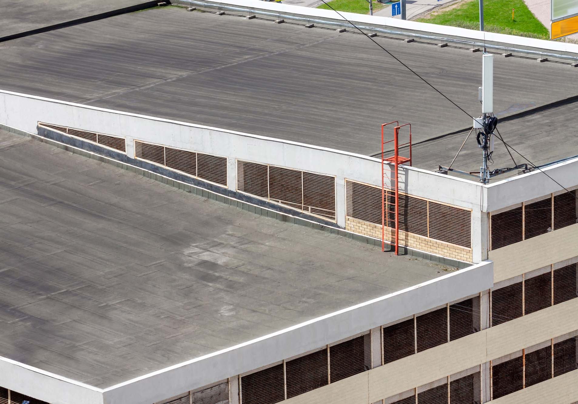 Flat roof top modern commercial building car garage exterior mixed-use urban multi-family residential area. Flat roof top with antenna system and ladder on modern commercial building car garage facade residential area for sale. Urban development concept image